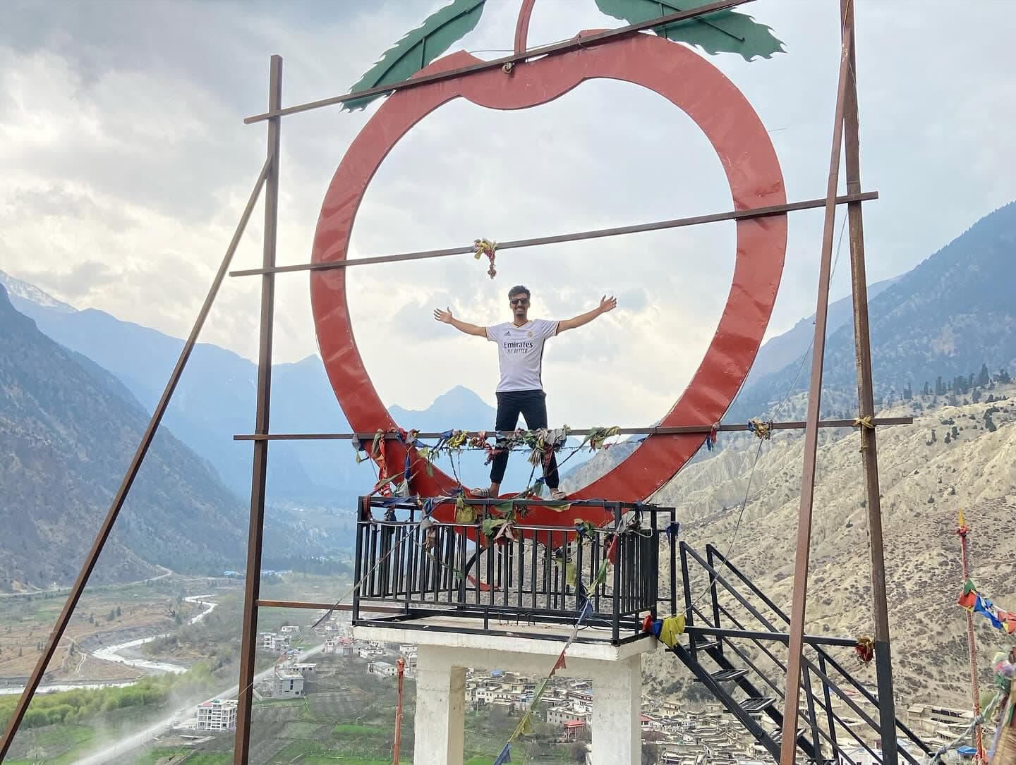 Subarna Poudel standing with arms outstretched inside a large apple-shaped sculpture on a mountain viewing platform.