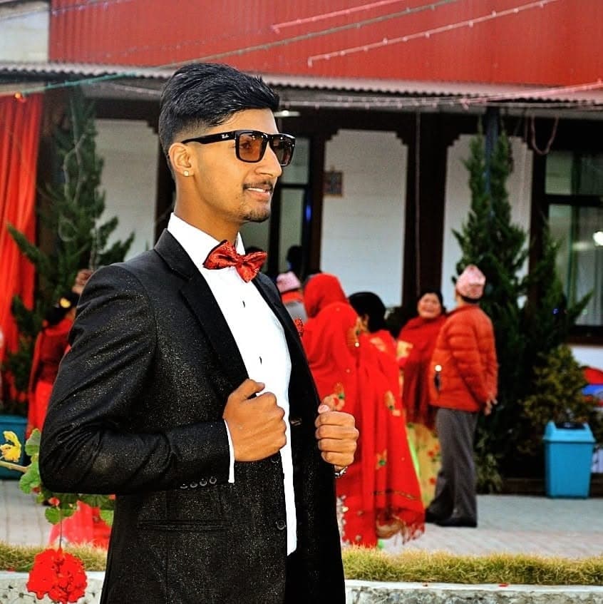 Subarna Poudel in a dark tuxedo and red bow tie at an outdoor evening function.